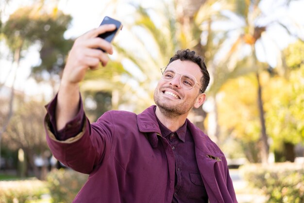 Hombre caucásico joven al aire libre haciendo un selfie con teléfono móvil