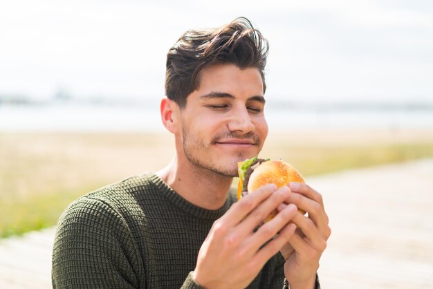 Hombre caucásico joven al aire libre sosteniendo una hamburguesa