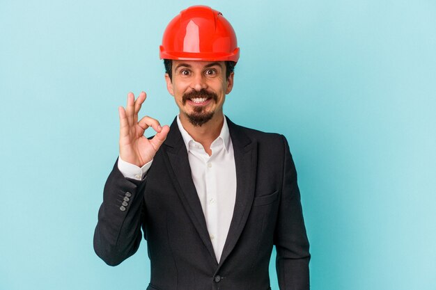 Hombre caucásico joven arquitecto aislado sobre fondo azul alegre y confiado mostrando gesto ok.