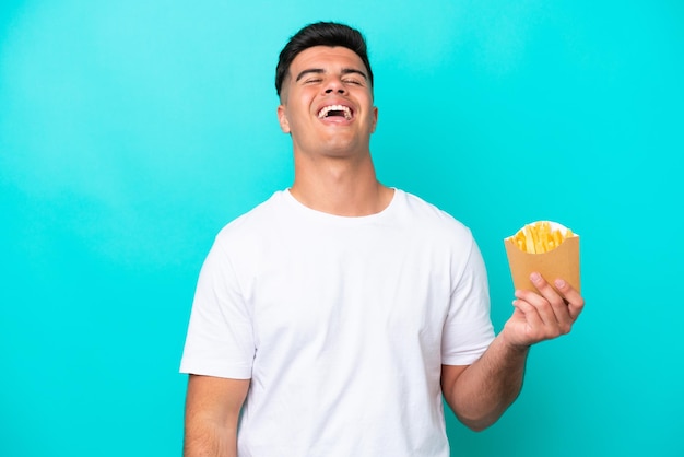 Hombre caucásico joven atrapando papas fritas aislado sobre fondo azul riendo