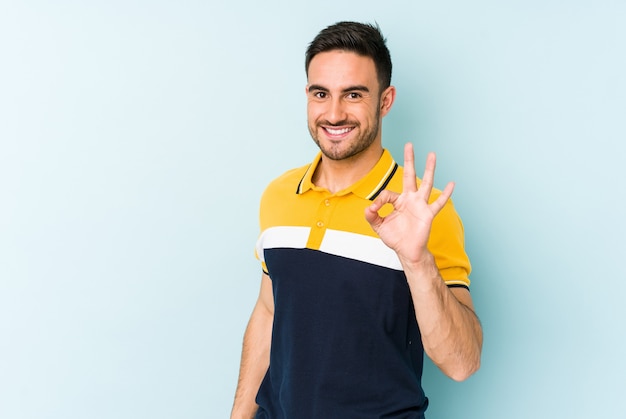 Hombre caucásico joven en azul alegre y confiado mostrando gesto ok.