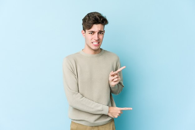 Hombre caucásico joven en azul sorprendido apuntando con los dedos índices a un espacio de copia.