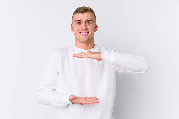 Hombre caucásico joven en blanco sosteniendo algo con ambas manos, presentación del producto.