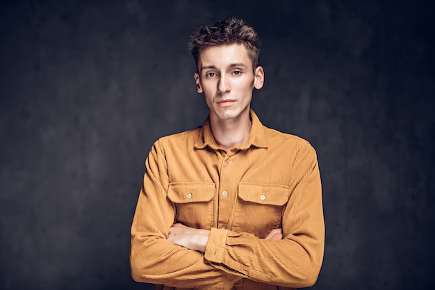 Hombre caucásico joven con los brazos cruzados sobre fondo gris oscuro