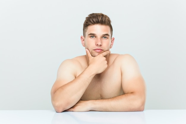 Hombre caucásico joven sin camisa sentado.