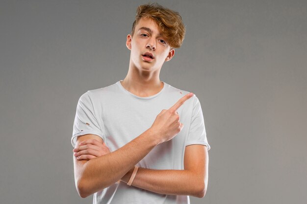 Hombre caucásico joven en camiseta blanca posando y gesticulando aislado en la pared gris