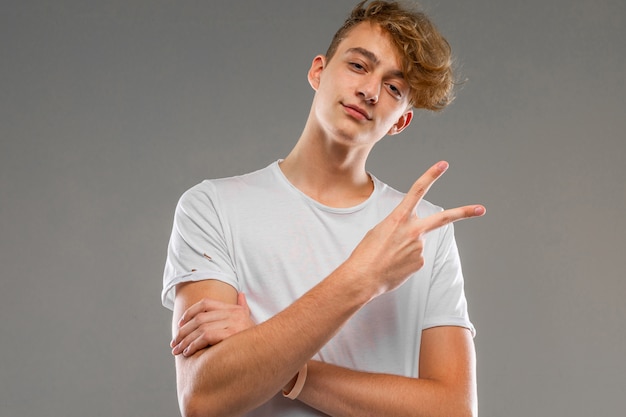 Hombre caucásico joven en camiseta blanca posando y gesticulando aislado en la pared gris