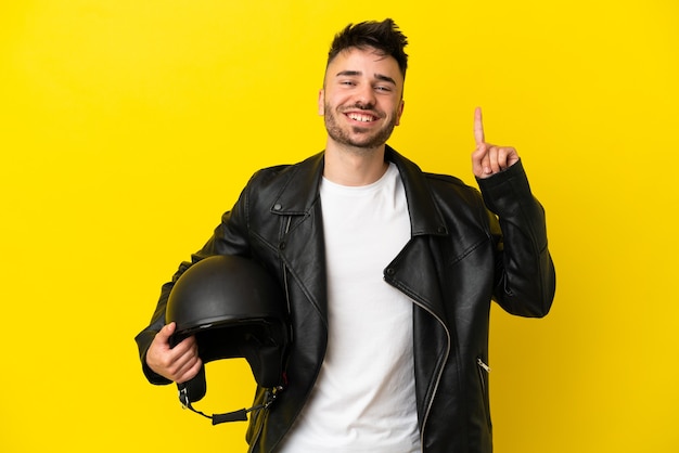 Hombre caucásico joven con un casco de motocicleta aislado sobre fondo amarillo apuntando hacia una gran idea