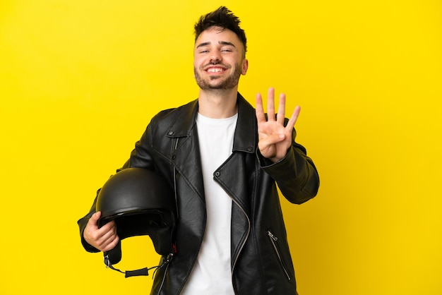 Hombre caucásico joven con un casco de motocicleta aislado sobre fondo amarillo feliz y contando cuatro con los dedos