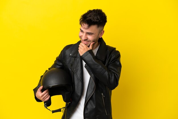 Hombre caucásico joven con un casco de motocicleta aislado sobre fondo amarillo mirando hacia el lado y sonriendo