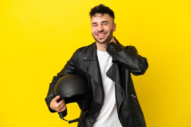 Hombre caucásico joven con un casco de motocicleta aislado sobre fondo amarillo riendo