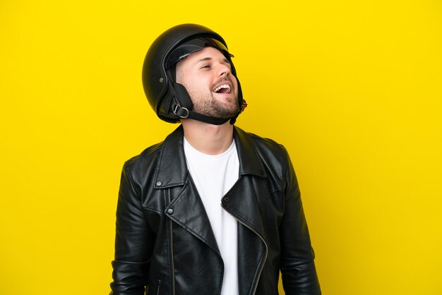 Hombre caucásico joven con un casco de motocicleta aislado sobre fondo amarillo riendo