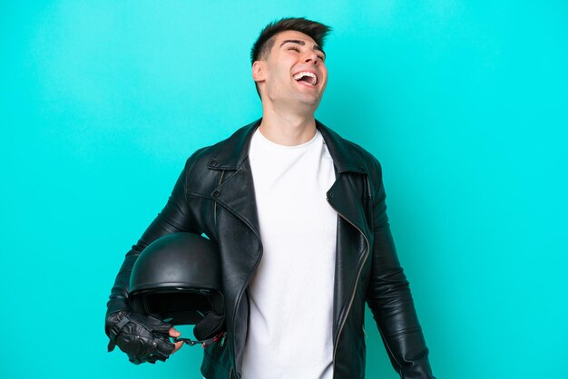 Hombre caucásico joven con un casco de motocicleta aislado sobre fondo azul riendo