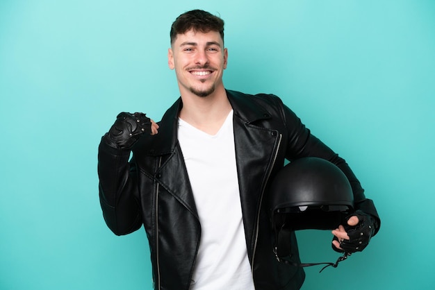 Hombre caucásico joven con un casco de motocicleta aislado sobre fondo azul riendo