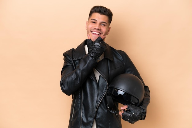 Hombre caucásico joven con un casco de motocicleta aislado sobre fondo beige feliz y sonriente