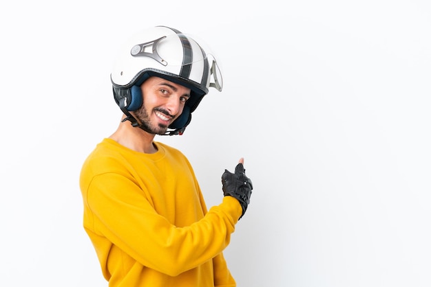 Hombre caucásico joven con un casco de motocicleta aislado sobre fondo blanco apuntando hacia atrás