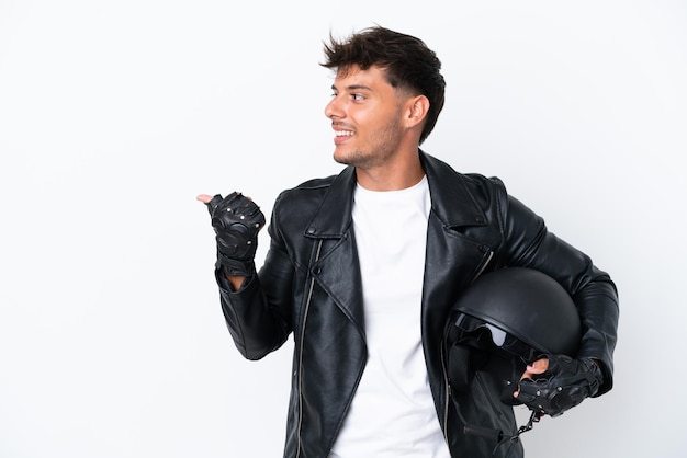 Hombre caucásico joven con un casco de motocicleta aislado sobre fondo blanco apuntando hacia el lado para presentar un producto