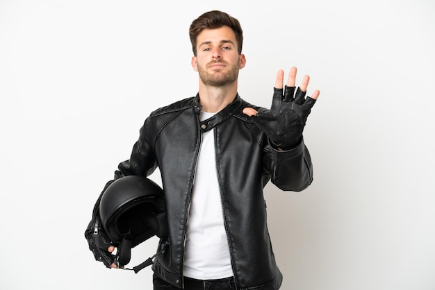 Hombre caucásico joven con un casco de motocicleta aislado sobre fondo blanco contando cinco con los dedos