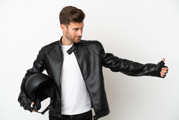 Hombre caucásico joven con un casco de motocicleta aislado sobre fondo blanco dando un gesto de pulgar hacia arriba