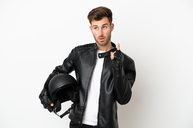 Hombre caucásico joven con un casco de motocicleta aislado sobre fondo blanco pensando en una idea apuntando con el dedo hacia arriba