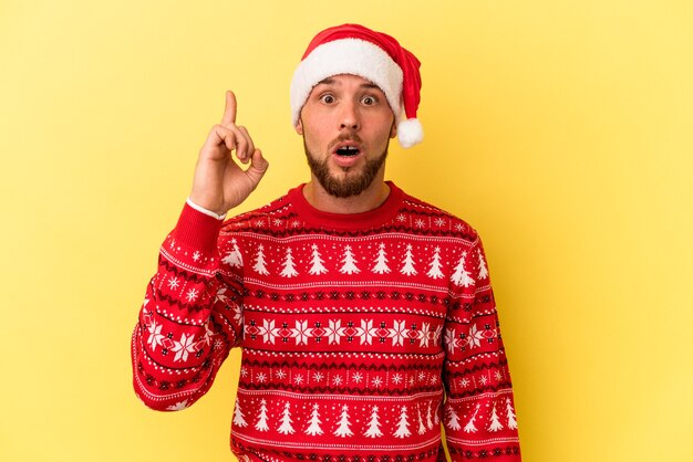 Hombre caucásico joven celebrando la Navidad aislado sobre fondo amarillo con una idea, concepto de inspiración.