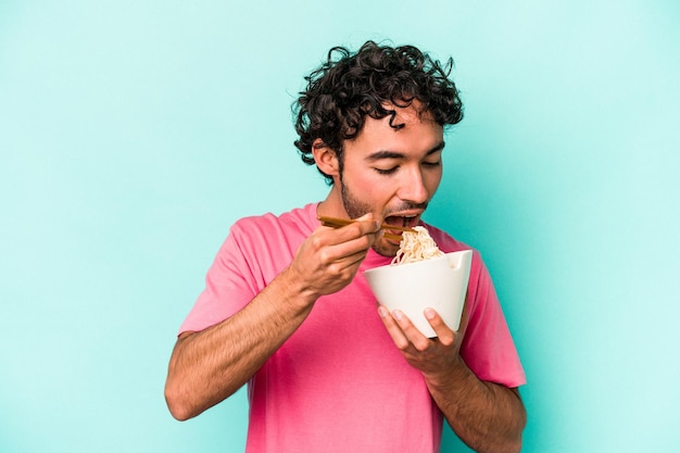 Hombre caucásico joven comiendo fideos aislado sobre fondo azul.