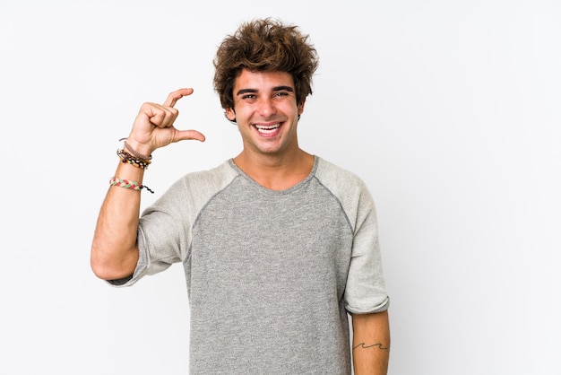 Hombre caucásico joven contra un blanco aislado sosteniendo algo poco con los dedos índices, sonriente y confiado.