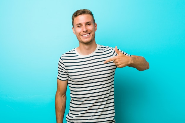 Hombre caucásico joven contra una persona de la pared azul que señala con la mano a una camisa copia espacio, orgulloso y confiado