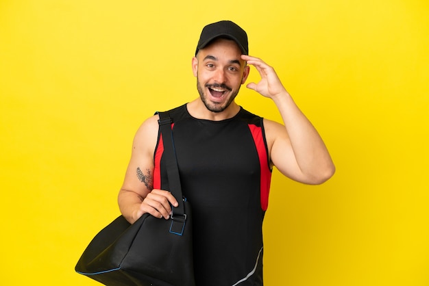Hombre caucásico joven deporte con bolsa de deporte aislado sobre fondo amarillo con expresión de sorpresa