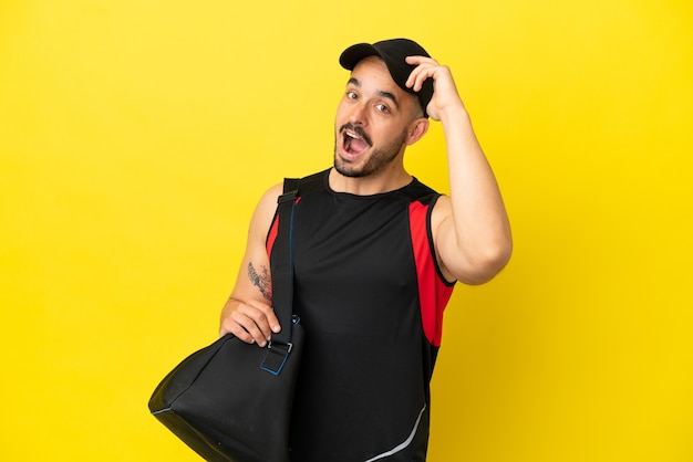 Hombre caucásico joven deporte con bolsa de deporte aislado sobre fondo amarillo haciendo gesto de sorpresa mientras mira hacia el lado