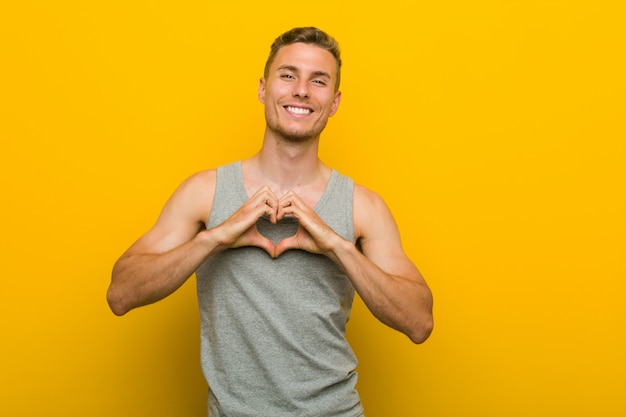 Hombre caucásico joven deporte sonriendo y mostrando una forma de corazón con las manos.