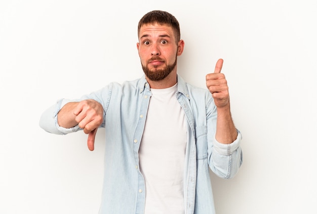 Foto hombre caucásico joven con diastema aislado sobre fondo blanco mostrando los pulgares hacia arriba y hacia abajo, concepto de elección difícil