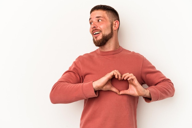 Foto hombre caucásico joven con diastema aislado sobre fondo blanco sonriendo y mostrando una forma de corazón con las manos.