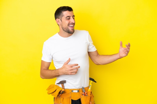 Hombre caucásico joven electricista aislado sobre fondo amarillo haciendo gesto de guitarra