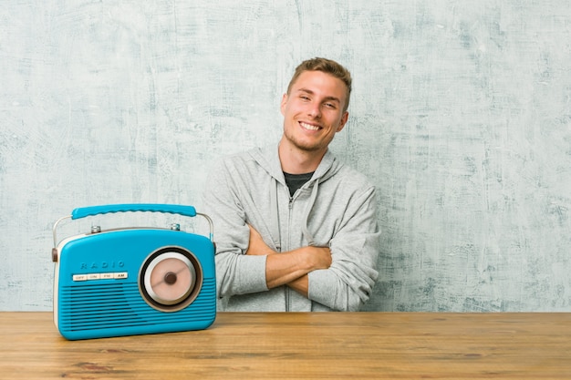 Hombre caucásico joven escuchando la radio sonriendo confiados con los brazos cruzados.