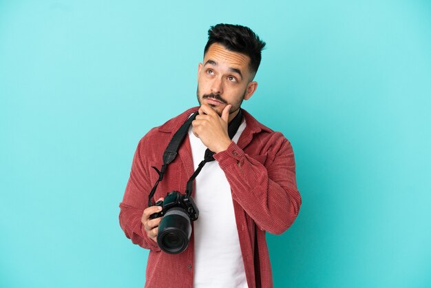 Hombre caucásico joven fotógrafo aislado sobre fondo azul que tiene dudas y con expresión de la cara confusa