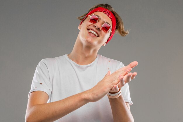 Hombre caucásico joven en gafas de sol rojas, camiseta blanca posando aislado en la pared gris