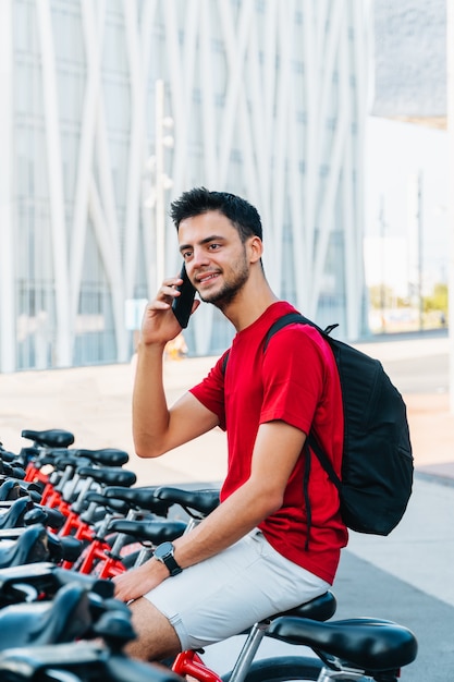 Hombre caucásico joven hablando por teléfono sentado en una bicicleta alquilada