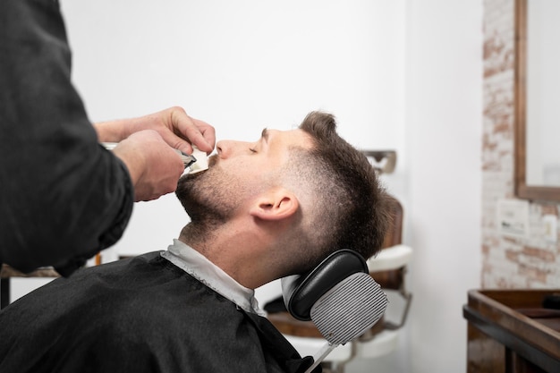 Hombre caucásico joven inconformista durante el arreglo de la barba en la peluquería moderna Peinado de hombres Hombre guapo obteniendo un nuevo peinado con recortadora eléctrica Fotografía de alta calidad