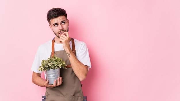 El hombre caucásico joven del jardinero que sostenía una planta aisló relajado pensando en algo que miraba un espacio de la copia.