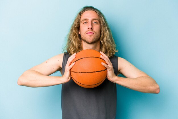 Hombre caucásico joven jugando baloncesto aislado sobre fondo azul.