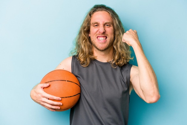 Hombre caucásico joven jugando baloncesto aislado sobre fondo azul.