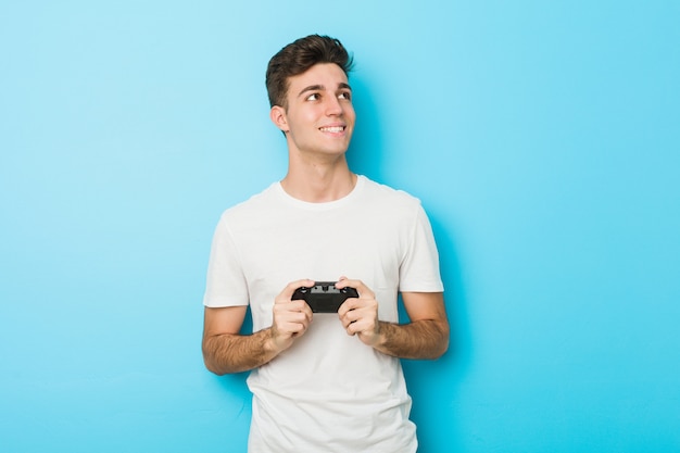 Hombre caucásico joven jugando videojuegos con controlador de juego sonriendo confiados con los brazos cruzados.