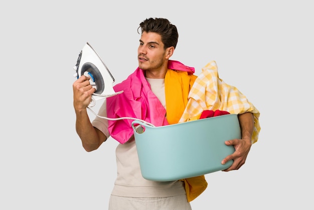 Foto hombre caucásico joven lavando la ropa y sosteniendo una plancha aislada