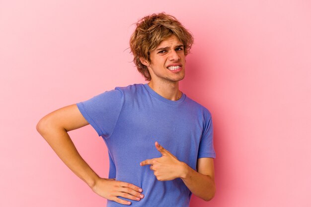 Hombre caucásico joven con maquillaje aislado sobre fondo rosa con dolor de hígado, dolor de estómago.