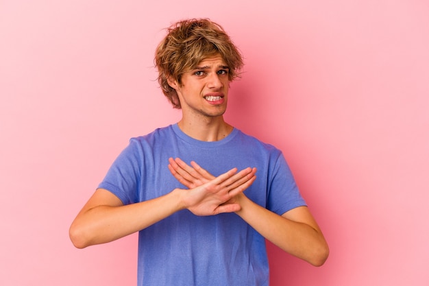Hombre caucásico joven con maquillaje aislado sobre fondo rosa haciendo un gesto de negación