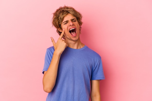 Hombre caucásico joven con maquillaje aislado sobre fondo rosa llorando, descontento con algo, concepto de agonía y confusión.