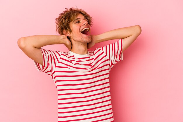 Hombre caucásico joven con maquillaje aislado sobre fondo rosa sintiéndose confiado, con las manos detrás de la cabeza.