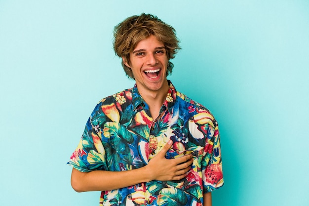 Hombre caucásico joven con maquillaje con ropa de verano aislado sobre fondo azul riendo y divirtiéndose.