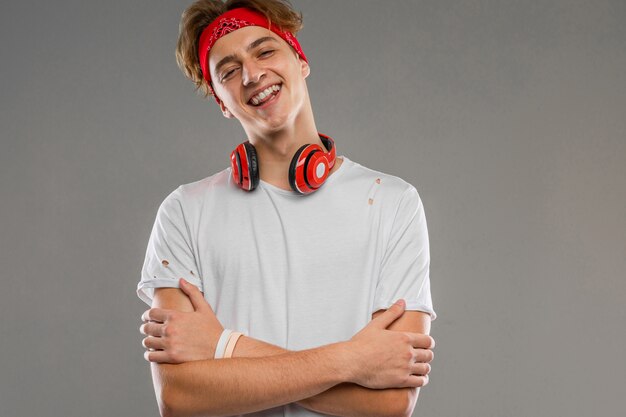 Hombre caucásico joven con el pelo corto y rizado rojo en camiseta blanca, gafas rojas, auriculares aislados sobre un fondo gris posando en la cámara